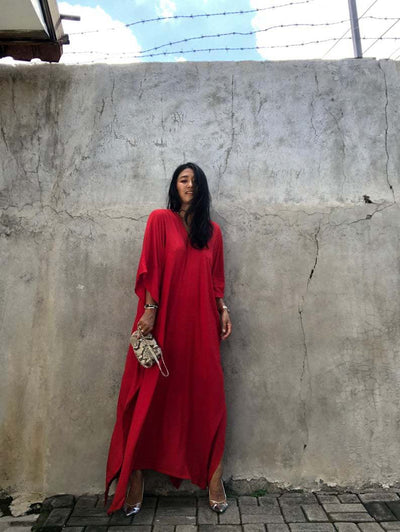 a woman in a red dress standing next to a wall 